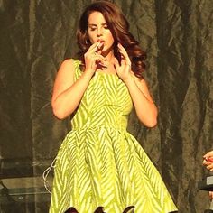 a woman in a yellow dress standing on stage with her hands clasped to her mouth