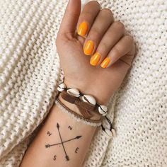 a woman with yellow nails is holding her arm up and wearing a bracelet that has two crossed arrows on it