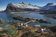 an aerial view of some houses and mountains in the water with snow capped peaks behind them