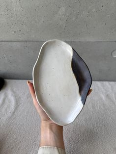 a hand holding a white and black plate on top of a bed next to a wall