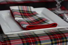 a plaid table cloth is folded on a white plate with silverware and wine glasses