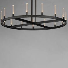 a large circular chandelier with candles hanging from the center, in front of a gray background