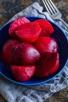 a blue bowl filled with red potatoes on top of a table next to a fork