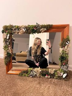 a woman sitting on the floor taking a selfie in front of a mirror with flowers