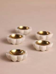 four white bowls with gold rims sitting on a pink tablecloth, one in the middle