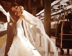 a bride and groom pose for a wedding photo in front of a train at the station