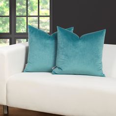 two teal pillows sitting on top of a white couch