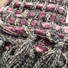 a close up view of a knitted blanket with pink and grey yarn on it