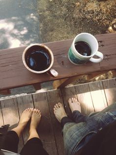 two people are sitting on a bench with their feet propped up next to coffee cups