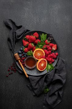 a plate filled with fruit, berries and honey on top of a black table cloth