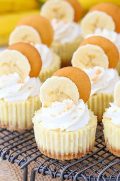 cupcakes with banana slices and whipped cream frosting are on a cooling rack