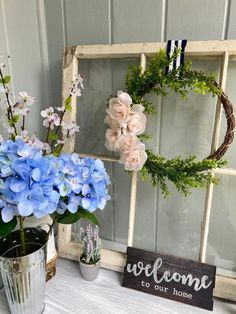 blue flowers and greenery sit in vases next to a sign that says welcome to our home