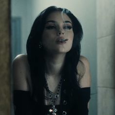 a woman with long black hair and piercings looking at herself in a bathroom mirror