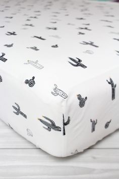 a close up of a bed with a white sheet and black cactus print on it