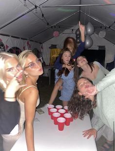 a group of people standing around a table with cups on it and balloons hanging from the ceiling