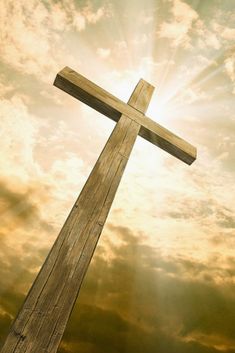 a wooden cross in front of a cloudy sky with the sun peeking through it's clouds