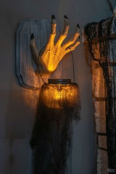 a light that is on the side of a wall next to a vase with hands coming out of it