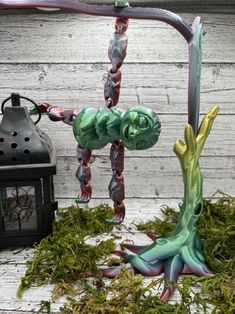 a green and purple sculpture sitting on top of a moss covered ground next to a lantern