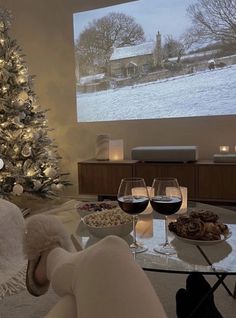 a person sitting in front of a christmas tree with wine glasses on the coffee table