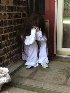 a person with long hair standing in front of a door and covering their face with her hands