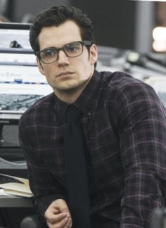 a man wearing glasses and a tie sitting at a desk