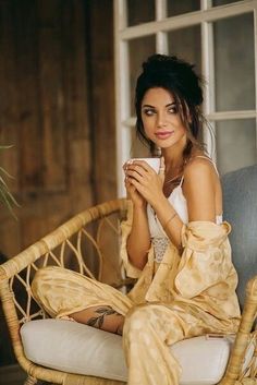 a woman sitting on a wicker chair holding a cup