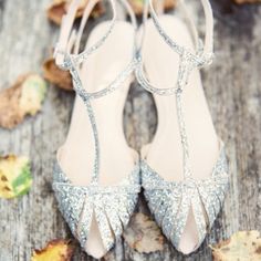 a pair of silver high heeled shoes sitting on top of a wooden floor covered in leaves