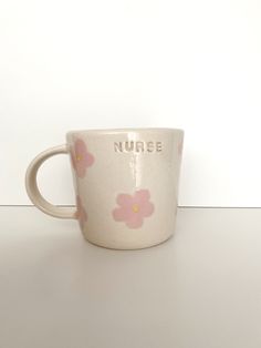 a white cup with pink flowers on it sitting on top of a table next to a wall