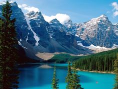 the mountains are covered in snow and pine trees, near a lake with blue water