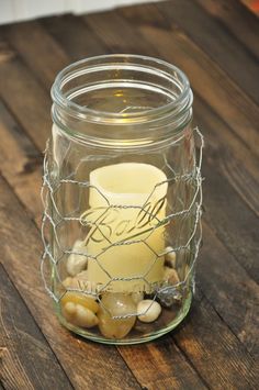 a glass jar filled with rocks and a lit candle on top of a wooden table