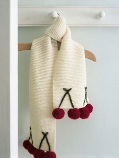 a white scarf hanging on a hook with red pom - poms attached to it