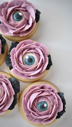 four cupcakes with pink frosting and blue eyes on them are arranged in the shape of roses