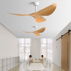 two people sitting at a table in a room with white walls and ceiling fans hanging from the ceiling