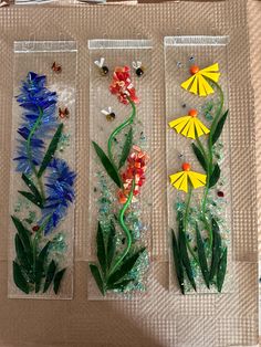 three glass vases with flowers in them sitting on top of a cardboard box filled with sand