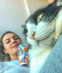 a woman laying in bed next to a black and white cat with a starbucks cup