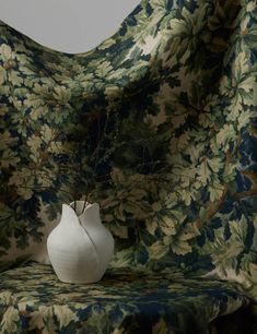 a white vase sitting on top of a couch covered in a floral print cover over it's back