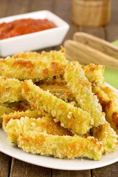 fried zucchini sticks on a white plate next to a bowl of chili sauce