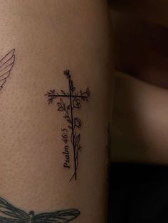 a cross and a dragonfly tattoo on the leg, with words written in cursive writing