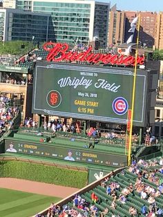 a baseball stadium filled with lots of people watching the game in progress on a big screen