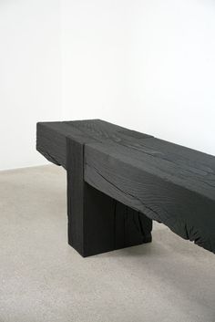 a wooden bench sitting on top of a cement floor next to a white walled wall