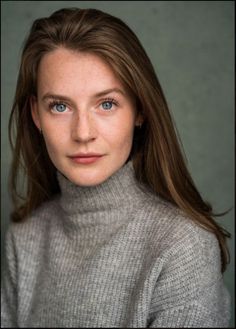 a woman with long hair and blue eyes posing for a photo in front of a gray background