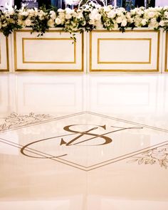 the floor is decorated with white flowers and gold trimmings, along with an elegant monogram