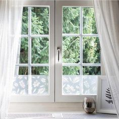 an open window with white curtains in front of it and a vase next to it