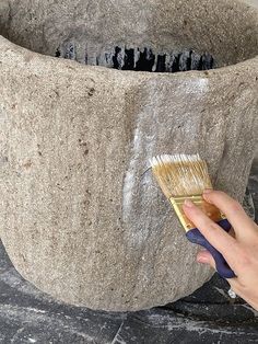 a hand holding a paintbrush over a large stone planter that is being used as a fountain