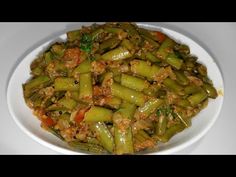 a white bowl filled with green beans and meat on top of a table next to a fork