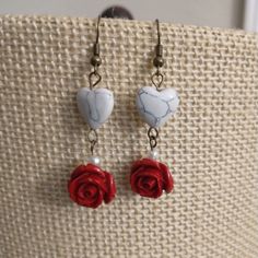 two red roses are attached to marble heart shaped earrings on a piece of fabric with pearls