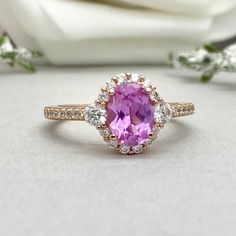 an oval shaped pink sapphire and diamond ring on a white cloth with flowers in the background