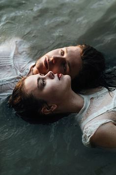 two people are floating in the water with their heads close to each other and one is wearing a white shirt