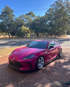 a pink sports car is parked on the side of the road in front of some trees