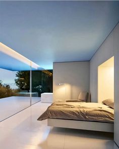 a modern bedroom with white walls and floor to ceiling windows overlooking the city at night